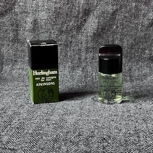 Könnte beinhalten: Eine kleine Glas-Parfümflasche und die passende Schachtel. Die Flasche hat einen schwarzen Deckel und einen transparenten Körper mit grüner Flüssigkeit. Die Schachtel ist grün und schwarz mit dem Text "Hurlingham eau de cologne for men ATKINSONS".