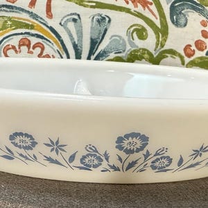 Peut inclure: Un plat à four ovale blanc cassé avec un motif floral bleu sur la base. Le plat a des poignées à chaque extrémité et est fait d'un matériau épais et opaque. Un article de cuisine vintage.