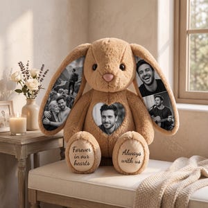 Op de afbeelding: Een lichtbruine pluche konijnenknuffel met zwart-wit fotoprints op de lange oren en een hartvormige patch op de borst. Op de voeten staat de tekst "Forever in our hearts" en "Always with us" geborduurd in een zwart handschrift.