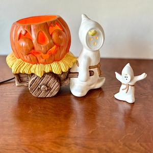 Set di decorazioni da tavolo vintage in ceramica per Halloween con fantasma che traina un carretto di zucche intagliate e luci, completo di statuetta di fantasma abbinata.