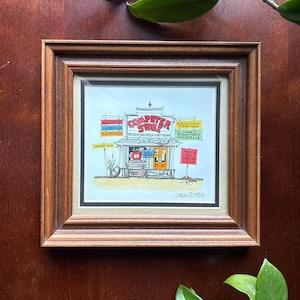 May include: A framed cartoon illustration of a computer store with a wooden storefront, orange door, and various signs including "Hardware," "Software," and "Memory Lane." The artwork is signed "Mason 1985" and features a detailed, colorful drawing.