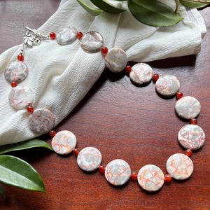 May include: A white ceramic mug with a black handle and the text "But First, Coffee" in a bold, black font. The mug is set against a blurred background, suggesting a cozy setting.