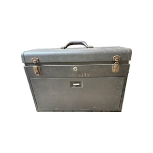 May include: A vintage, gray metal toolbox with a handle, latches, and a drawer. The toolbox has a keyhole and the text "KRV 4570" is visible. The overall design suggests a durable storage solution for tools or other items.