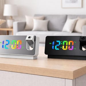 May include: Two digital alarm clocks with a projection feature. One clock is white with a mirrored face, the other is black. Both display the time in a rainbow of colors. The clocks sit on a light-colored wooden surface.