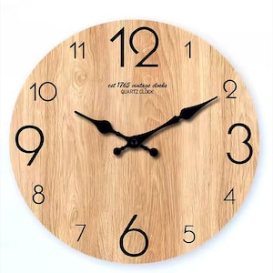 May include: A round wooden wall clock with black numerals and hands. The clock face has a light brown wood grain pattern. The text "est 1765 vintage clocks QUARTZ CLOCK" is printed near the center.