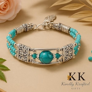 May include: A turquoise beaded bracelet with decorative silver-tone metalwork. The bracelet has a large turquoise stone and filigree details. The background is neutral with a rose and foliage.