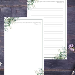 May include: Two white notepads with a green border and eucalyptus leaf accents. The text "I can do all things through Christ who strengthens me" and "Philippians 4:13" is printed on the notepads. The notepads are on a dark wood surface.