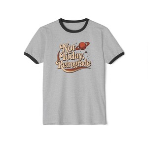 A gray t-shirt with a graphic design featuring the text "Not Today, Retrograde" and a planet-like symbol.