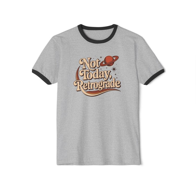 A gray t-shirt with a graphic design featuring the text "Not Today, Retrograde" and a planet-like symbol.