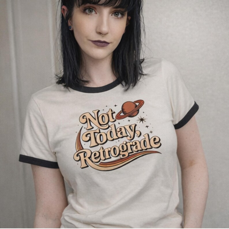 A woman wearing a white t-shirt with a graphic design that says "Not Today, Retrograde" and features a planet and stars.