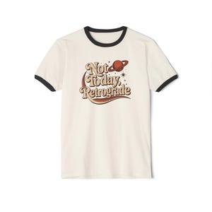 A white t-shirt with a black rim and a graphic design featuring the text "Not Today, Retrograde" along with a planet and stars.