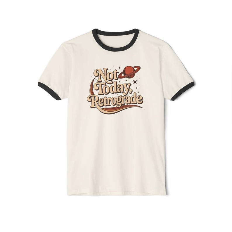 A white t-shirt with a black rim and a graphic design featuring the text "Not Today, Retrograde" along with a planet and stars.