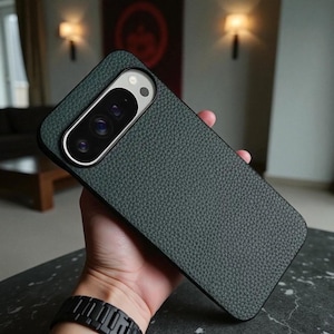 Può includere: Custodia per telefono strutturata verde scuro con modulo fotocamera argentato. La custodia ha un aspetto simile alla pelle ed è tenuta in mano. Il modulo fotocamera ha più lenti e un flash.