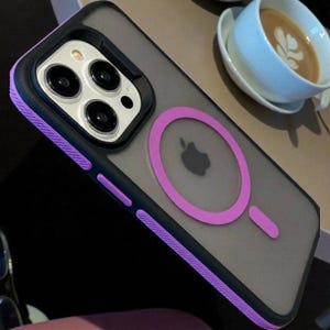 Puede incluir: Una funda transparente para teléfono con borde negro y detalles morados. La funda presenta un anillo magnético morado y un logotipo de Apple. La funda está diseñada para un teléfono inteligente con múltiples lentes de cámara.