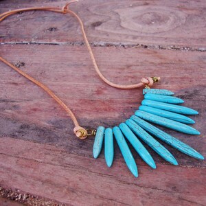 May include: A turquoise blue necklace with a leather cord and a fan-shaped pendant made of turquoise stones.