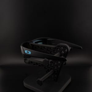 May include: Black sunglasses with a blue accent on the frame, displayed on a black stand. The sunglasses have a sleek, modern design. The stand has a geometric pattern.