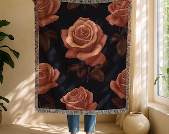 May include: A dark blue throw blanket with a repeating pattern of large, detailed roses in peach and brown. The blanket has a fringed edge. The roses have intricate details. The blanket is held up by a person.