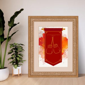 Puede incluir: Obra de arte enmarcada con una pancarta roja con una ilustración de guantes de boxeo dorados. La pancarta tiene ribetes y texto dorados. El fondo tiene salpicaduras de acuarela rojas, naranjas y blancas. El marco es dorado.