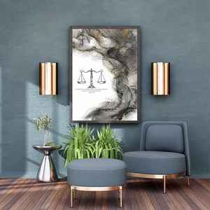 May include: A framed abstract art print with a balance scale illustration and text, in a room with a blue chair, ottoman, and wall sconces. The artwork features black, white, and gold tones. The room has a modern, minimalist design.