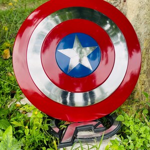 May include: A red, silver, and blue Captain America shield. The shield has a red outer ring, a silver middle ring, and a blue center with a white star. The shield is a replica of the one used by the superhero.