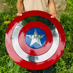 May include: A red, white, and blue shield with a star in the center. The shield is round with a silver band and a blue circle in the middle. The outer ring is red.