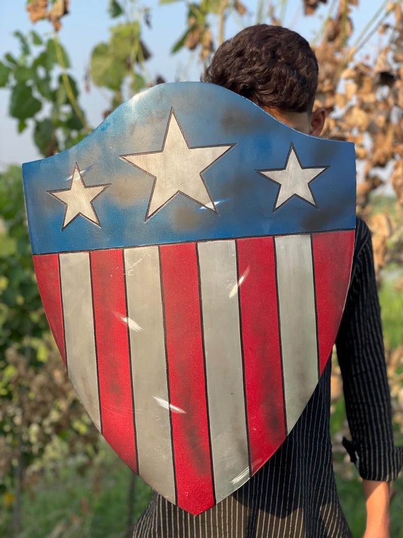 Op de afbeelding: Een schild met een blauw bovenstuk met drie witte sterren. Het onderste gedeelte heeft rode en witte verticale strepen. Het schild is een patriottisch ontwerp.