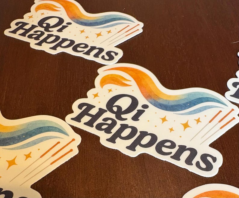 May include: White stickers with the text "Qi Happens" in a dark blue font. The stickers feature a colourful design with orange, blue, and yellow accents, along with gold stars and acupuncture needles. The stickers are on a brown surface.