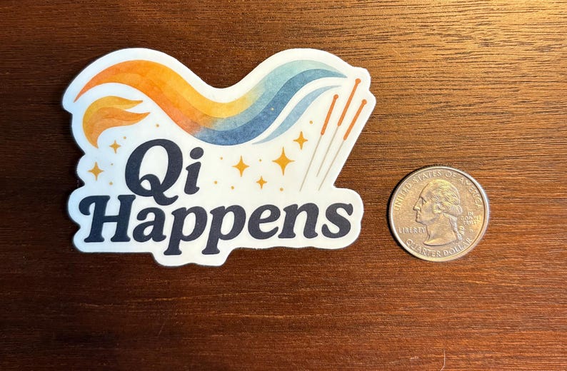 May include: A white sticker with the text "Qi Happens" in navy blue, featuring a colourful design of orange, yellow, and blue waves, with gold stars and acupuncture needles. A quarter coin is next to the sticker.