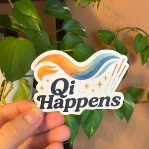 May include: A sticker with the text "Qi Happens" in a navy blue font. The sticker features a colourful design with orange, yellow, and blue waves, along with several gold stars and acupuncture needles.