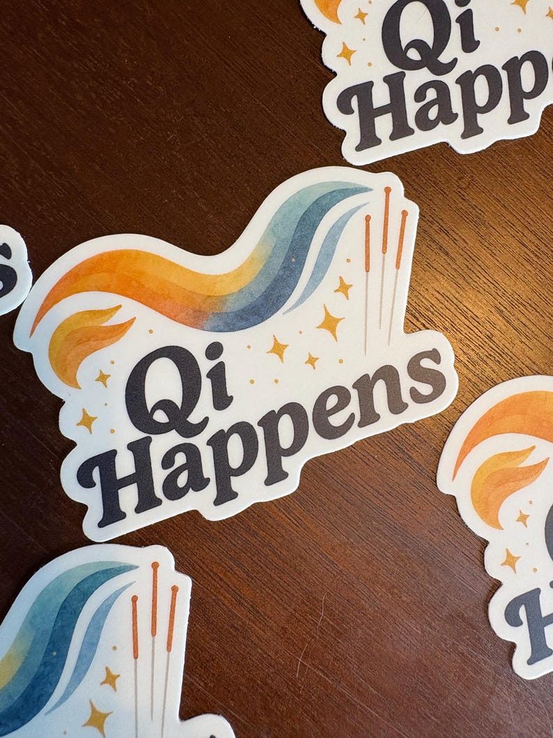 May include: White stickers with the text "Qi Happens" in black, featuring a colourful wave design in orange, blue, and yellow, with gold star accents and acupuncture needles. The stickers are on a brown wooden surface.