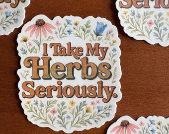 May include: White stickers with the text "I Take My Herbs Seriously" in brown, surrounded by floral illustrations. The stickers feature a variety of flowers in shades of pink, blue, and yellow, with green foliage. The stickers are on a brown surface.