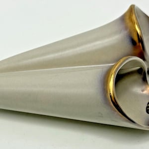 Peut inclure: Deux vases muraux en céramique en forme de cône allongé avec une finition gris clair lisse. Chaque vase présente une large ouverture avec un bord doré métallique et des nuances sombres et fumées. Un cordon tressé marron est attaché.