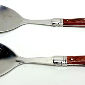 Peut inclure: Un ensemble de service à salade en acier inoxydable, comprenant une cuillère et une fourchette. Les manches sont en bois brun rougeâtre avec des détails argentés. L'ensemble est conçu pour servir des salades.