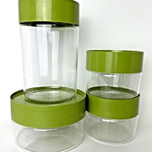 Peut inclure: Ensemble de quatre bocaux en verre transparent avec des couvercles et des bandes vert vif. Les bocaux sont de hauteurs et de tailles variables, adaptés au stockage en cuisine. Les couvercles sont vert opaque.