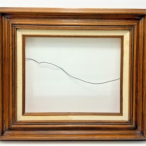 May include: A rectangular wooden picture frame with a dark brown finish and a light beige fabric liner. The frame features a stepped, tiered moulding design and includes a thin black metal hanging wire stretched across the open centre area.