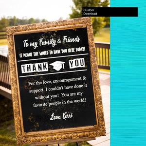May include: A framed chalkboard sign with gold trim, displaying white text on a black background. The text reads "To my Family & Friends," "THANK YOU," and a personal message. A graduation cap graphic is included. The sign is propped on a wooden easel.