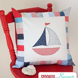 May include: A cushion with a sailboat design. The cushion has a white centre with a blue and red sailboat applique. The edges are trimmed with patchwork fabric in various blue, red, and white patterns. The text "Sail Away Pillow" is at the top.