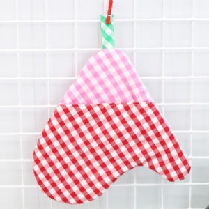 Puede incluir: Dos guantes de horno de cuadros rojos y blancos, un guante de horno de cuadros rosa y blancos, un guante de horno de cuadros verdes y blancos, dos cápsulas para cupcakes rojas y blancas, una jarra blanca, dos huevos, un batidor de alambre y un tarro de vidrio verde con tapa de corcho.