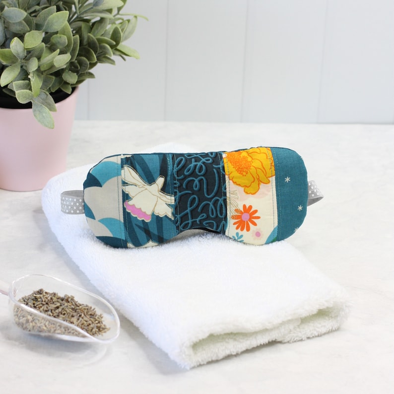 May include: A blue and white eye mask with a floral pattern. The mask is made of fabric and has a gray elastic band.