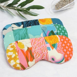May include: Three colorful eye masks made of patchwork fabric. The masks are in shades of blue, green, pink, orange, and yellow. The fabric has a variety of patterns, including floral, geometric, and abstract designs.