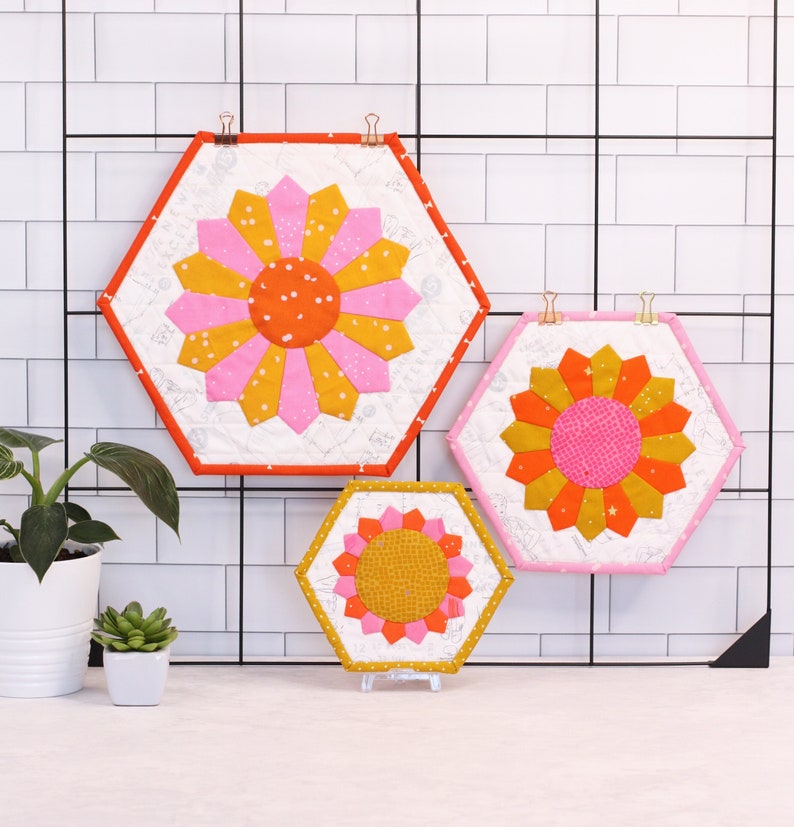 A set of three Dresden placemats. Placemat are hexagon shaped and are small, medium and large. They feature a big, bright, colourful dresden plate in the centre.