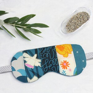May include: A blue and white eye mask with a floral and abstract pattern. The mask is made of fabric and has a white elastic strap.