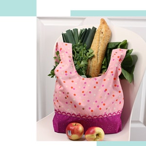 May include: Pink reusable shopping bag with white polka dots and a purple trim. The bag is filled with groceries, including a baguette, leeks, and parsley. Two red apples are in front of the bag. The text "Eco Shopper" is at the top of the image and "a SPOONFUL of Sugar" is at the bottom.