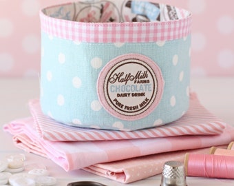 Peut inclure: Un panier de rangement en tissu bleu et blanc à pois avec une bordure rose à carreaux et une étiquette marron et blanche qui indique "Half Milk Farms Chocolate Dairy Drink Pure Fresh Milk".