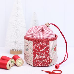 Pode incluir: Uma bolsa de tecido feita &agrave; m&atilde;o com uma parte superior xadrez vermelha e branca e um design de patchwork. O patchwork apresenta padr&otilde;es florais e florestais vermelhos e creme. Um cord&atilde;o vermelho e pequenas tesouras vermelhas tamb&eacute;m s&atilde;o vis&iacute;veis.