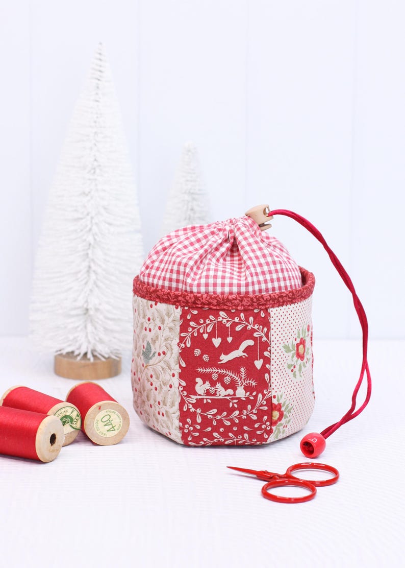 Pode incluir: Uma bolsa de tecido feita &agrave; m&atilde;o com uma parte superior xadrez vermelha e branca e um design de patchwork. O patchwork apresenta padr&otilde;es florais e florestais vermelhos e creme. Um cord&atilde;o vermelho e pequenas tesouras vermelhas tamb&eacute;m s&atilde;o vis&iacute;veis.