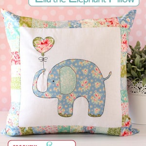 Puede incluir: Una almohada blanca con un diseño de patchwork con tela floral. La almohada tiene un elefante bordado sosteniendo un globo en forma de corazón. El texto "Ella the Elephant Pillow" está en la parte superior de la imagen y "a SPOONFUL of Sugar" está en la parte inferior.