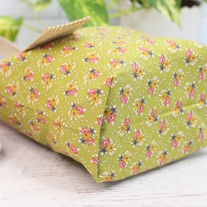 K&ouml;nnte beinhalten: Eine kleine gr&uuml;ne Stofftasche mit Blumenmuster. Die Tasche hat einen wei&szlig;en und braunen karierten Stoffgriff.