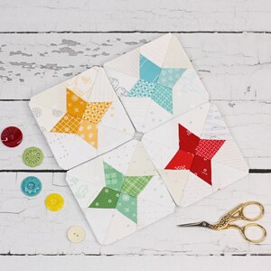 May include: Five fabric squares featuring a star design in various colours. The stars are constructed from smaller fabric pieces sewn together. The squares are arranged in a circle with the points of the stars facing outwards.