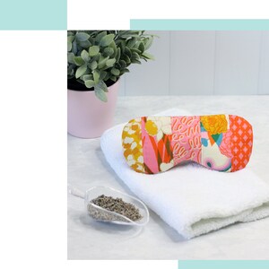 May include: A colorful patchwork eye pillow with a white background and pink, orange, yellow, and green floral patterns. The eye pillow is on a white towel with a small scoop of dried lavender next to it.